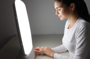 A person sitting at a table using a light box for morning phototherapy to boost energy and mood.